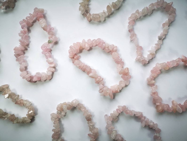 May include: A collection of pink rose quartz chip bracelets. The bracelets are made of small, irregular pieces of rose quartz that are strung together on elastic.