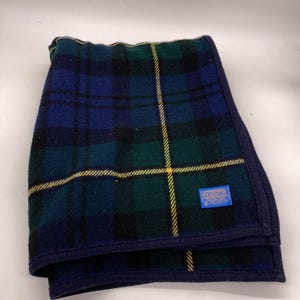 Puede incluir: Una manta de cuadros azules y verdes con una raya amarilla y una etiqueta azul que dice "Pendleton Woolen Mills, Portland, Oregon".