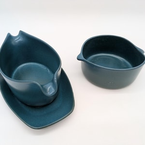 Può includere: Una salsiera in ceramica color verde acqua scuro con base integrata e una ciotola in ceramica abbinata. Entrambi i pezzi presentano una finitura opaca liscia con bordi curvi e un design interno profondo e arrotondato per servire salse.