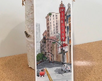 May include: A watercolor illustration of a city street scene with a red sign that reads "Fox Oakland" and a red car driving down the street.