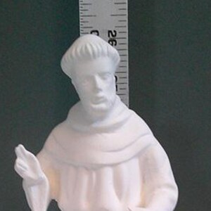 Könnte beinhalten: Eine weiße Keramikstatue einer religiösen Figur, möglicherweise eines Heiligen oder Mönchs, in einem langen Gewand und einer Kapuze. Die Figur steht auf einem abgerundeten Sockel. Die Statue ist etwa 25 cm hoch.