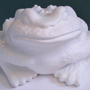 May include: A large, white ceramic frog sculpture. The frog is depicted in a seated position with a smiling expression. The sculpture has a textured surface and detailed features, including the frog's eyes, mouth, and limbs. The frog is sitting on a white surface.