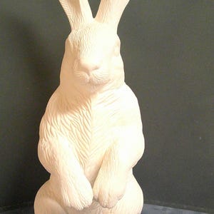 May include: A white ceramic rabbit figurine in a standing pose. The rabbit has long ears, a detailed face, and is holding its paws together. The figurine is approximately 30 cm tall.