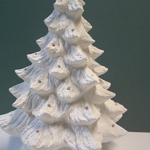 Könnte beinhalten: Ein weißer Weihnachtsbaum aus Keramik mit strukturierter Oberfläche. Der Baum hat mehrere Astschichten mit kleinen Löchern für Lichter. Der Sockel ist rund und ebenfalls weiß. Eine festliche Weihnachtsdekoration.