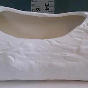 May include: A white ceramic planter shaped like a log, featuring a textured surface with a hollowed-out center. The planter measures approximately 12 inches long. Ideal for displaying small plants or succulents.