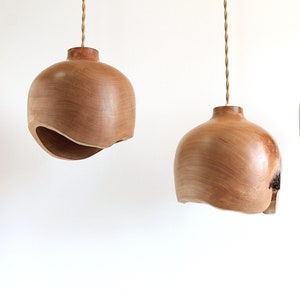 Può includere: Tre lampade a sospensione in legno con un design asimmetrico unico. Ogni lampada è realizzata in un unico pezzo di legno e ha una finitura naturale e calda.