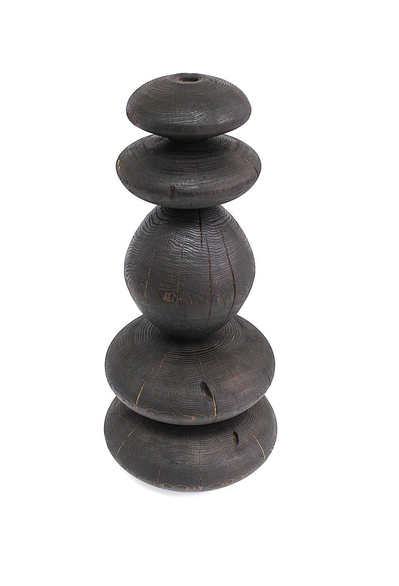 May include: A dark brown wooden sculpture composed of stacked, rounded shapes. The sculpture has a textured surface with visible wood grain and knots. The design features a series of varying sized, disc-like forms, creating a unique, abstract aesthetic.