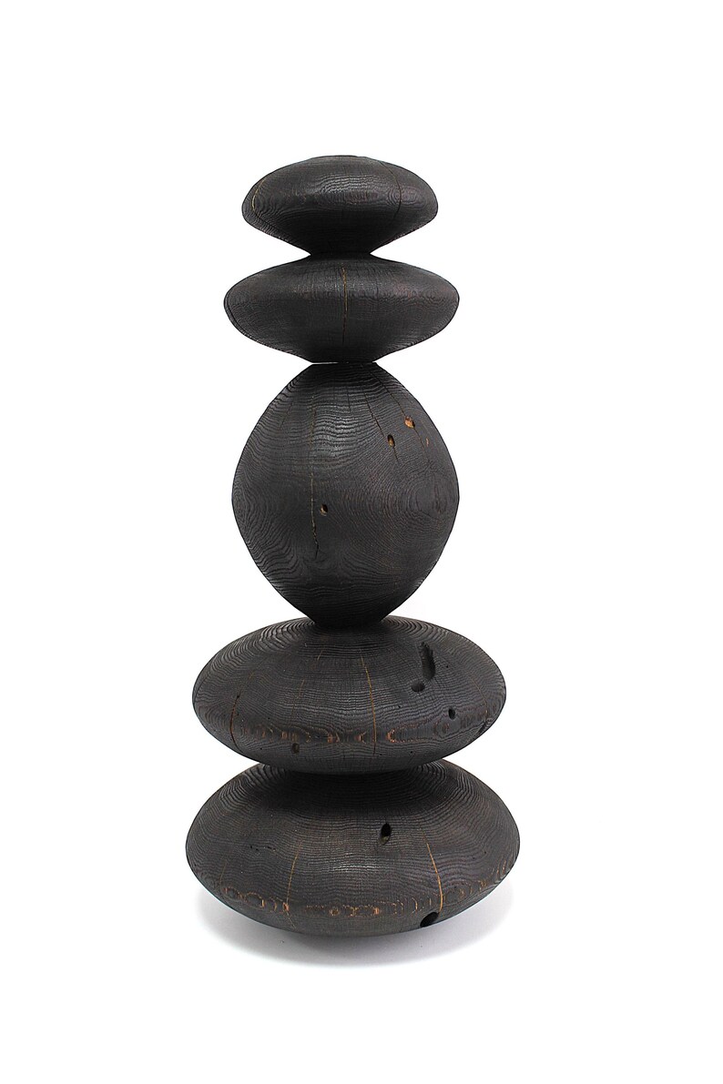 May include: A tall, dark wooden sculpture composed of stacked, rounded shapes. The sculpture has a natural, organic aesthetic, with visible wood grain and a charred finish. The arrangement of the shapes creates a balanced, eye-catching design, suitable for home decor.
