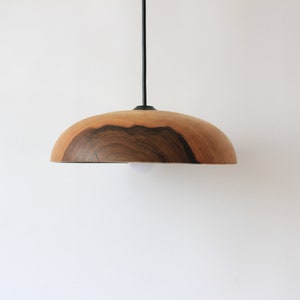 May include: A wooden pendant light with a natural wood finish and a dark brown wood grain pattern. The light is suspended from a black cord.