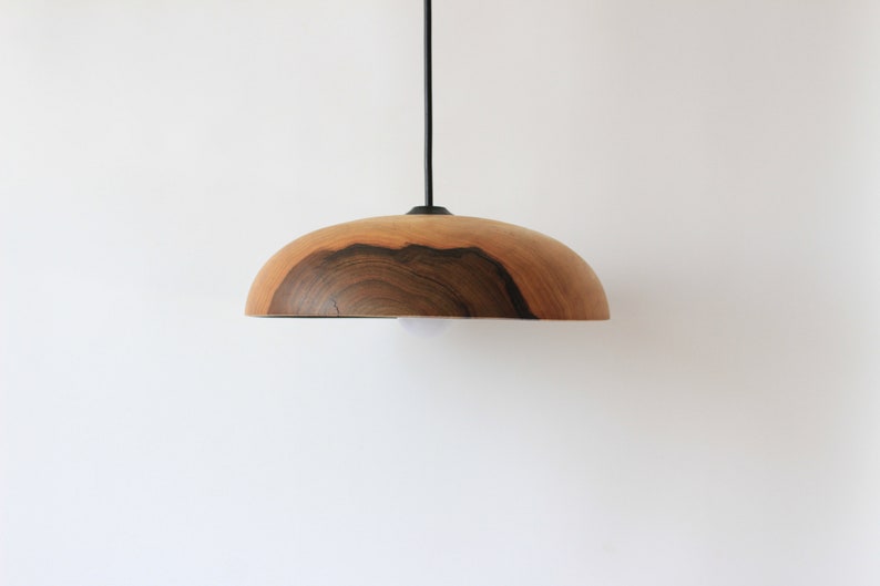 May include: A wooden pendant light with a natural wood finish and a dark brown wood grain pattern. The light is suspended from a black cord.