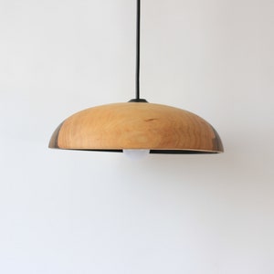 May include: A wooden pendant light with a natural wood finish and a black cord. The light fixture has a rounded, dome-shaped shade.