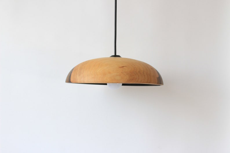 May include: A wooden pendant light with a natural wood finish and a black cord. The light fixture has a rounded, dome-shaped shade.