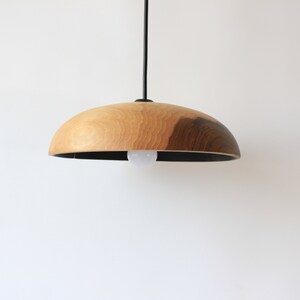 May include: A wooden pendant light with a natural wood finish and a black cord. The light has a round, dome-shaped shade.