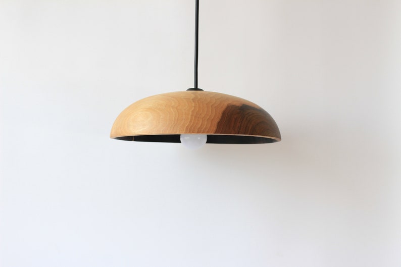 May include: A wooden pendant light with a natural wood finish and a black cord. The light has a round, dome-shaped shade.