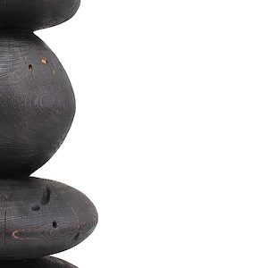 May include: A tall, dark wooden sculpture with a stacked, organic form. The sculpture is made of dark, possibly charred, wood, with a visible grain and natural imperfections. The design features rounded, stacked elements, creating a unique, abstract shape.