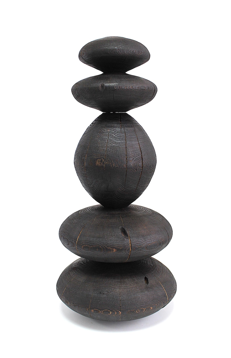 May include: A dark stained wooden sculpture composed of stacked, rounded shapes. The sculpture has a natural wood grain texture and a smooth, polished finish. The design is abstract and modern, suitable for home decor.