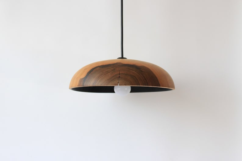May include: A wooden pendant light with a dark wood grain pattern and a black metal cord. The light fixture has a round, dome-shaped shade.