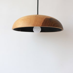 May include: A wooden pendant light with a black interior and a natural wood exterior. The light is hanging from a black cord.