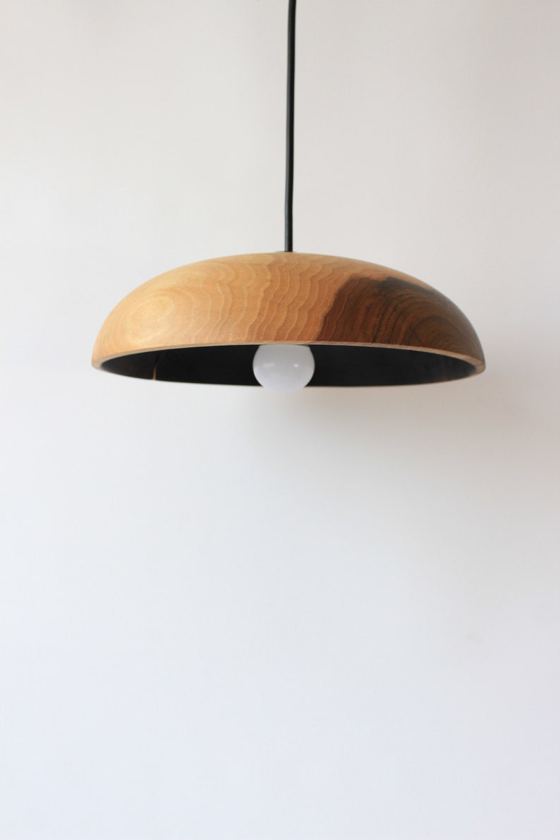 May include: A wooden pendant light with a black interior and a natural wood exterior. The light is hanging from a black cord.