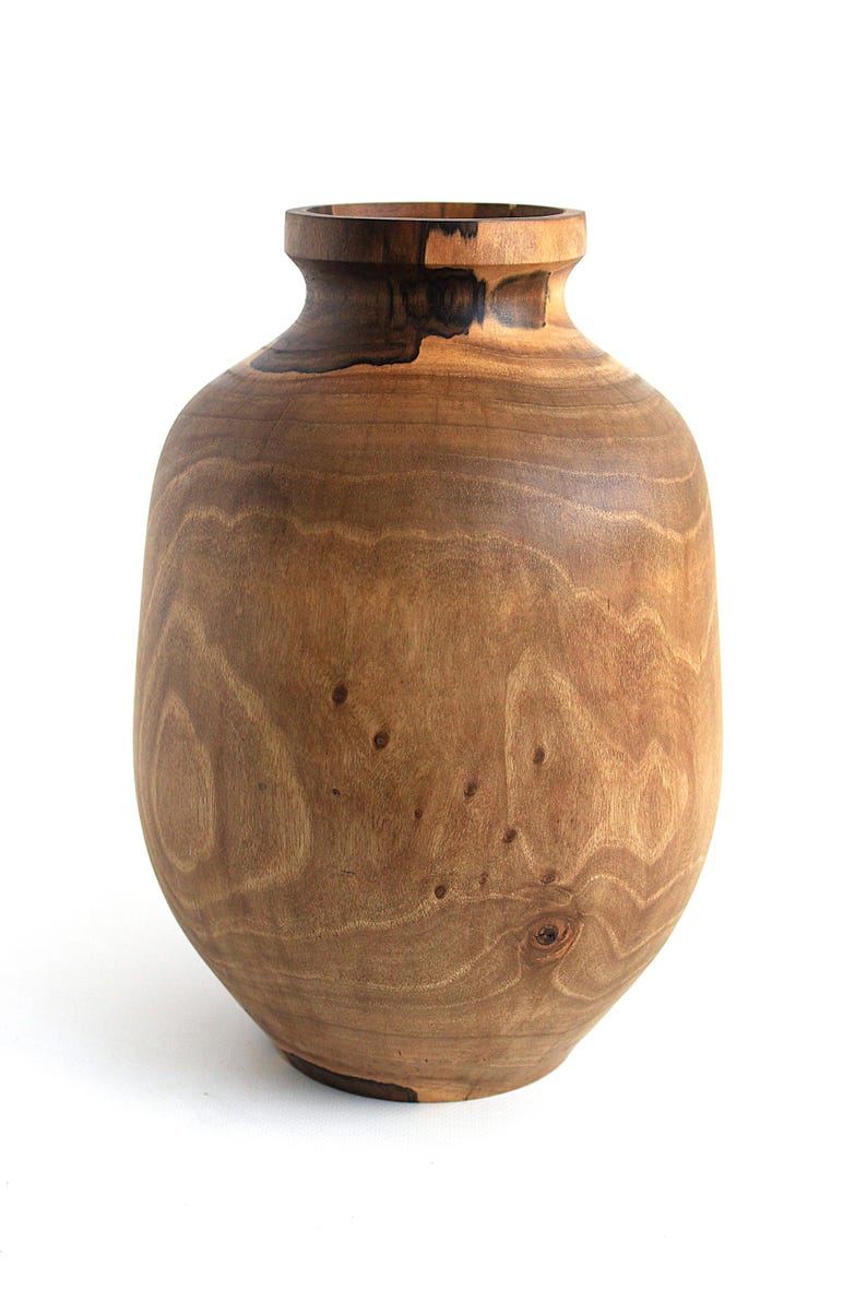 May include: A handcrafted wooden vase with a rounded body and a narrow neck. The vase is made of light brown wood with darker brown accents and visible wood grain. The vase is a decorative item.