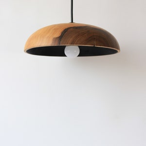 May include: A wooden pendant light with a black cord and a black interior. The light is made of natural wood with a dark brown grain.