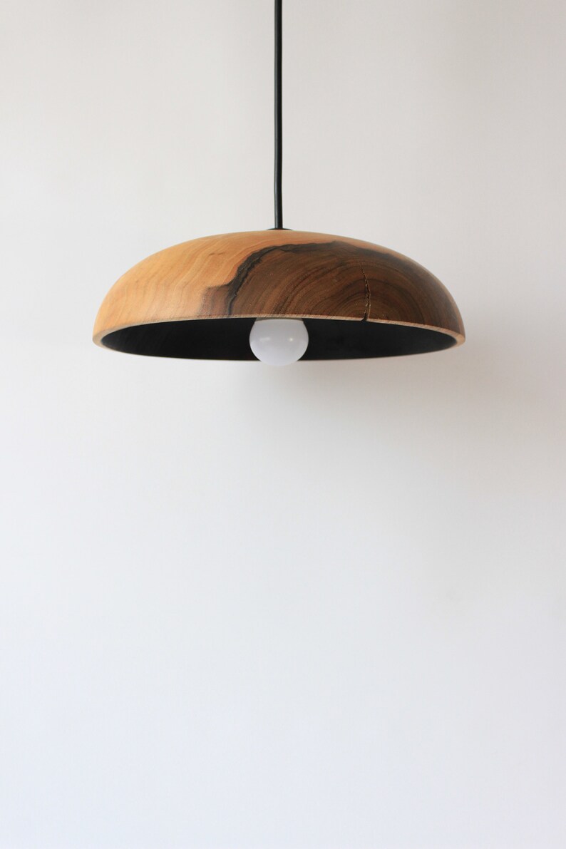 May include: A wooden pendant light with a black cord and a black interior. The light is made of natural wood with a dark brown grain.
