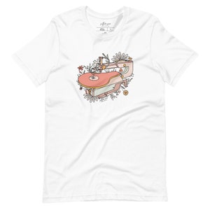 Peut inclure: Un t-shirt blanc avec une illustration rose et blanche d'un tourne-disque vintage entouré de fleurs. Le texte "J'espère que tu danses" est écrit sur le tourne-disque.