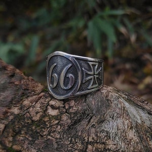 May include: A silver ring with the number "66" and a cross design. The ring is on a piece of weathered wood.