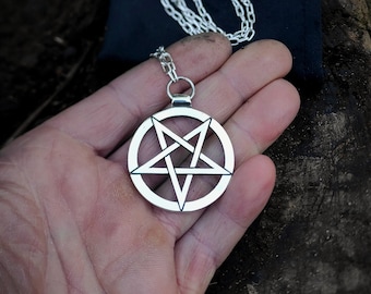 May include: A silver chain necklace with a pentagram pendant. The pendant is a five-pointed star with a circle around it.