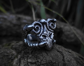 May include: A silver ring with a detailed design of a skull with horns. The ring is sitting on a piece of weathered wood.