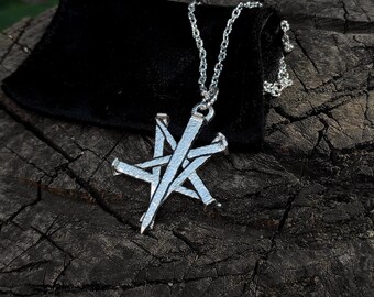 May include: A silver necklace with a five-pointed star pendant made of nails. The necklace is on a dark brown wooden surface.