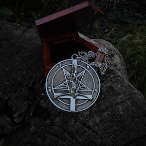 May include: A silver pendant necklace with a pentagram design featuring a figure in the center. The pendant is hanging open in a wooden box.