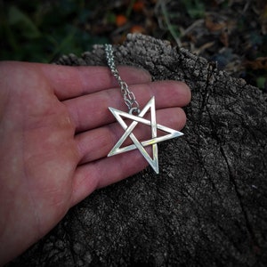 May include: A silver pendant necklace featuring a five-pointed star with an intricate design. The star is a pentagram, a symbol with a long history of use in various cultures and religions.