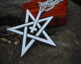 May include: A silver pendant necklace featuring a pentagram with an inverted cross in the center. The necklace is displayed on a wooden box.