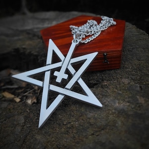 May include: A silver pendant necklace featuring a pentagram with an inverted cross in the center. The necklace is displayed on a wooden box.