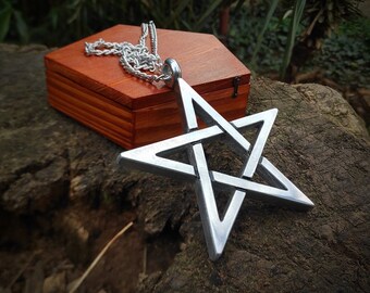 May include: A silver pentagram pendant necklace with a chain. The pendant is in the shape of a five-pointed star with a knot design. The necklace is resting on a wooden box.