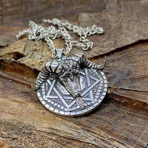 May include: Silver pendant necklace featuring a ram's head with horns and a pentagram star inside a circle with an inscription. The pendant is on a silver chain.
