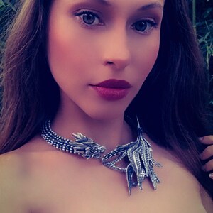May include: A woman wearing a silver dragon necklace with a black lace top.