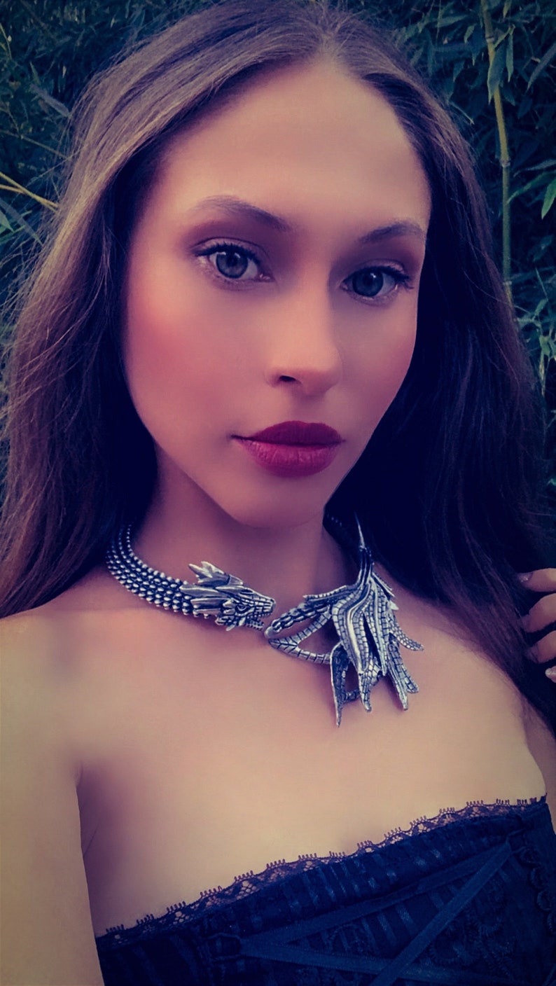 May include: A woman wearing a silver dragon necklace with a black lace top.
