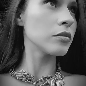 May include: A woman wearing a silver dragon necklace with a detailed design. The necklace features a dragon head on one side and a wing-like design on the other.