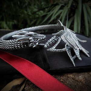 May include: Silver dragon head choker necklace with a detailed, textured design. The necklace is open in the back and has a dragon head on each end.