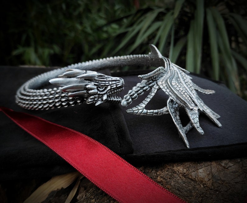 May include: Silver dragon head choker necklace with a detailed, textured design. The necklace is open in the back and has a dragon head on each end.
