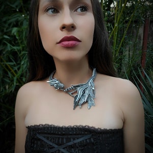 May include: A woman wearing a black strapless top with a silver dragon necklace. The necklace features a detailed dragon head and wings.
