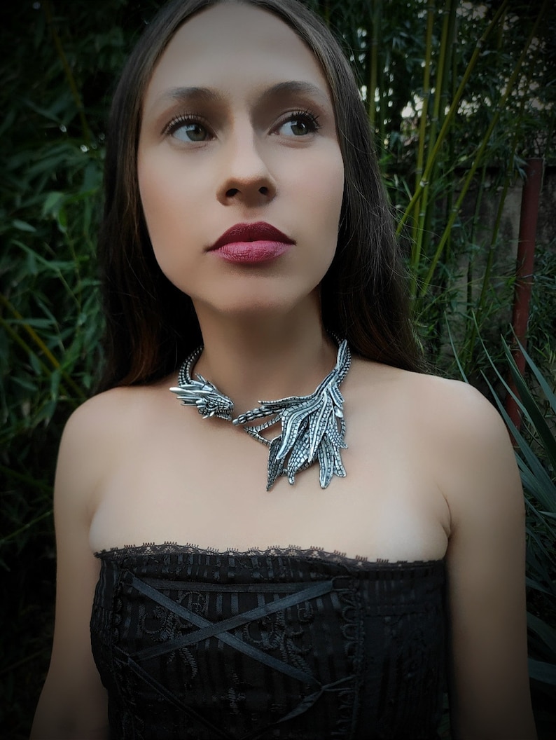 May include: A woman wearing a black strapless top with a silver dragon necklace. The necklace features a detailed dragon head and wings.