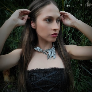 May include: A woman with long brown hair wearing a black corset top and a silver dragon necklace. The necklace has a detailed design with wings and a head.