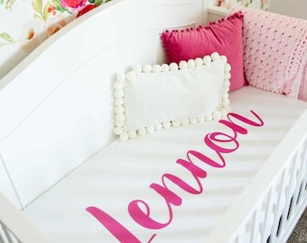 Può includere: Biancheria da letto per culla bianca con un motivo floreale rosa e il nome "Lemon" scritto in corsivo rosa.