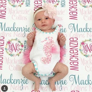May include: A baby girl wearing a white onesie with a pink and white seahorse design and a pink tulle skirt. The onesie has a blue and white striped trim. The baby is lying on a white blanket with the name "Mackenzie Collins" repeated in pink and blue lettering.