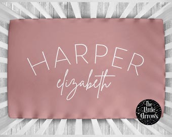 Può includere: Un lenzuolo con angoli rosa per lettino con il nome "HARPER elizabeth" stampato in bianco.