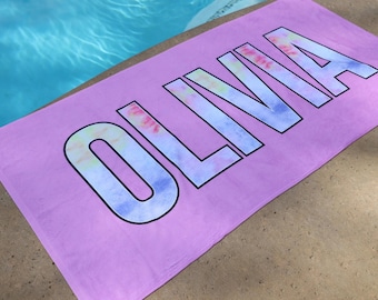 May include: A pink beach towel with the name "OLIVIA" printed in large, white letters with a tie-dye pattern.