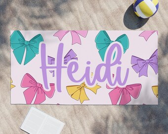 May include: A pink beach towel with a pattern of colourful bows and the name "Heidi" written in purple.